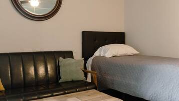 Een kamer met een bed, een ronde spiegel, een zwarte leren bank en een houten salontafel.