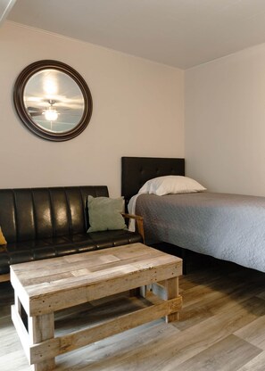 A room with a bed, a round mirror, a black leather sofa, and a wooden coffee table.