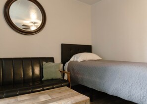 A room with a bed, a sofa, a small table, and a mirror on the wall.