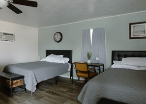 A hotel room with two beds, a desk, a chair, a clock, and a window with curtains.