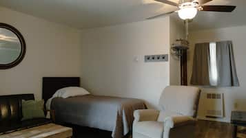 A bedroom with a bed, a chair, a wooden bench, a ceiling fan, and a window with curtains.