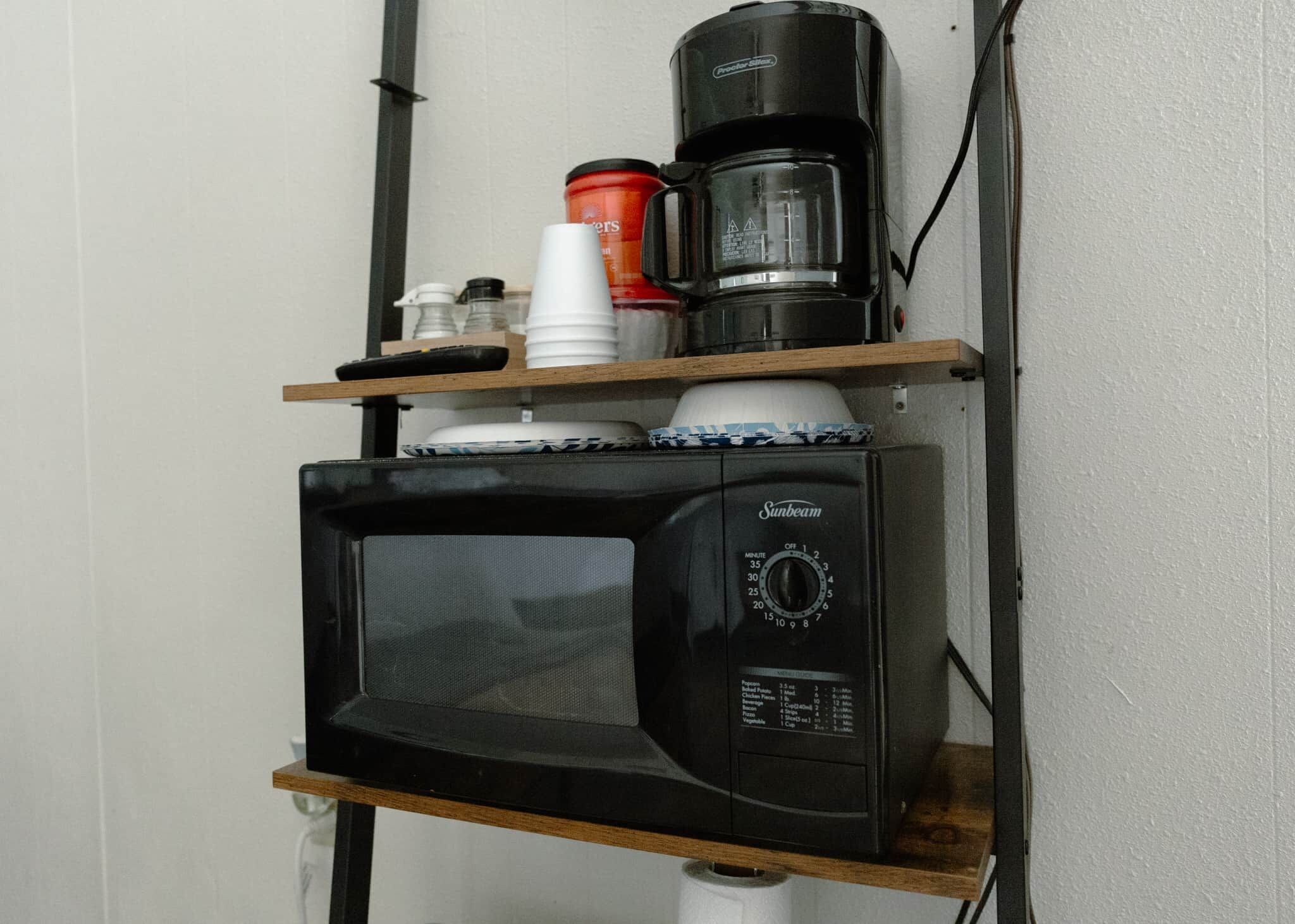 Un four à micro-ondes est posé sur une étagère, avec une machine à café et un récipient sur le dessus.