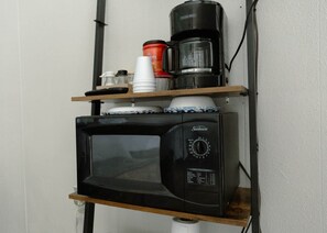 A microwave oven on a shelf with a coffee maker and a container on top. - Motel Room 4 – 2 Queens + Twin (Mobridge)