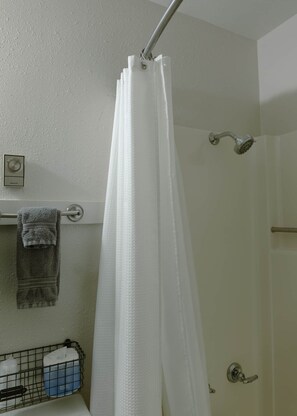 A shower area with a white shower curtain, a towel rack with a towel, and a showerhead.