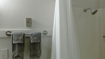 A bathroom with a towel rack holding two towels, a showerhead, and a thermostat on the wall.