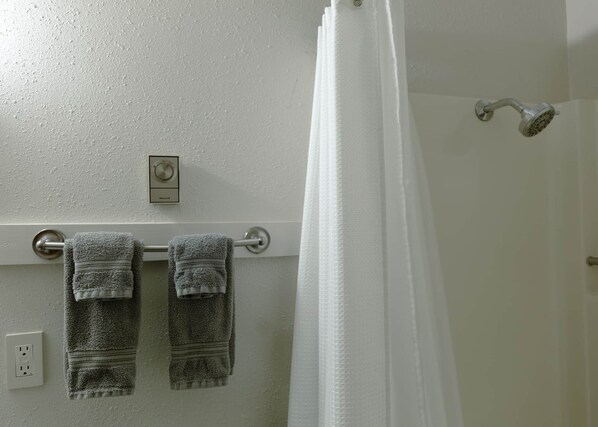 A bathroom with a towel rack holding two towels, a showerhead, and a thermostat on the wall.