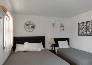 A hotel room with two beds, a round wall shelf with plants, a wall-mounted lamp, and a decorative metal piece.
