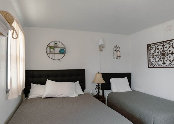A hotel room with two beds, a round wall shelf with plants, a wall-mounted lamp, and a decorative metal piece.