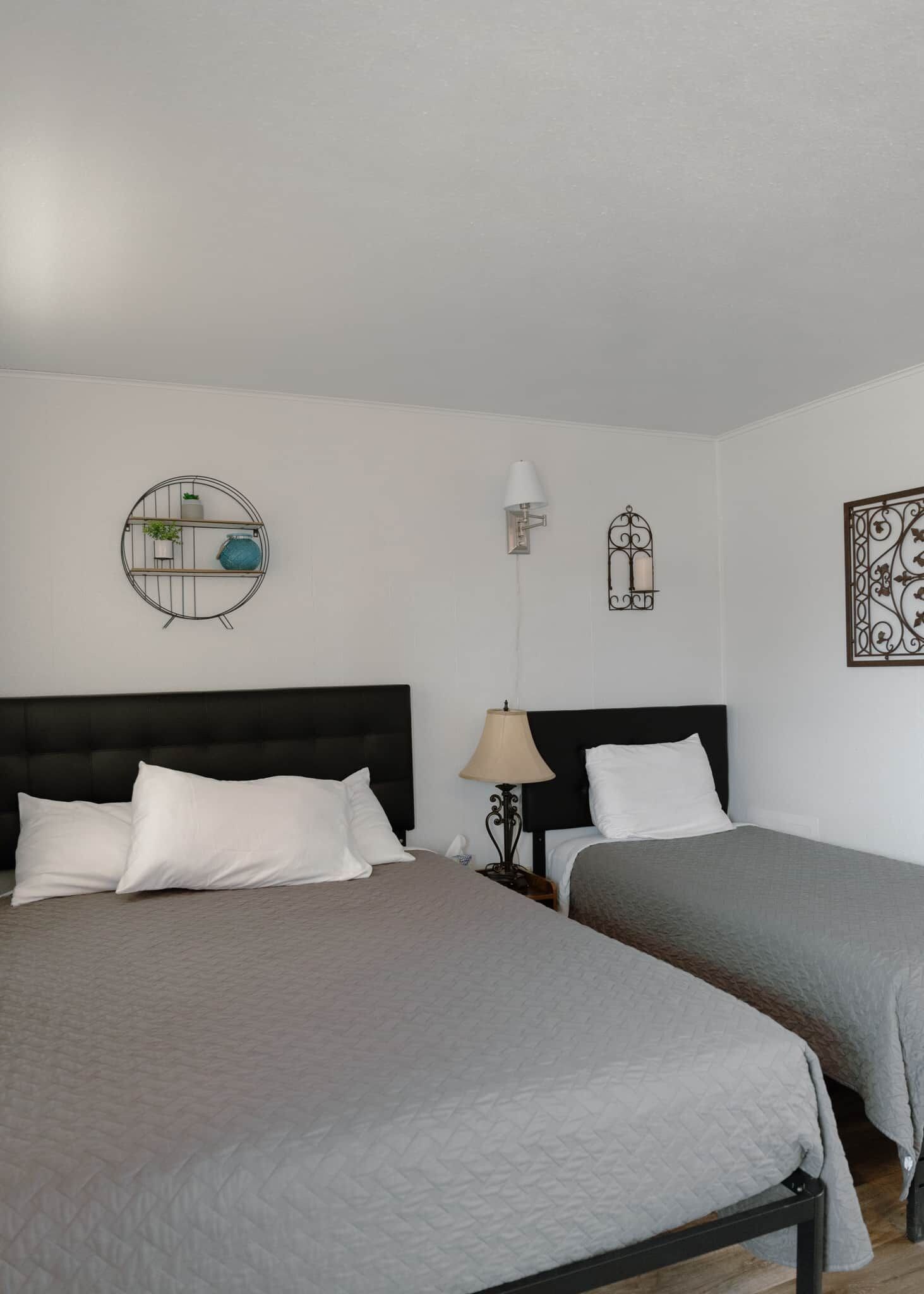 Une chambre d’hôtel avec deux lits, une étagère murale ronde ornée de plantes, une lampe fixée au mur et des œuvres d’art décoratives accrochées au mur.