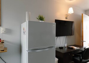 Cozinha compacta equipada com geladeira, um vaso pequeno com planta, televisão de tela plana e escrivaninha com cadeira.