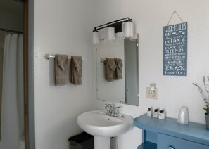 A bathroom with a white sink, a mirror, and a towel rack with towels. There is a sign on the wall with motivational phrases.