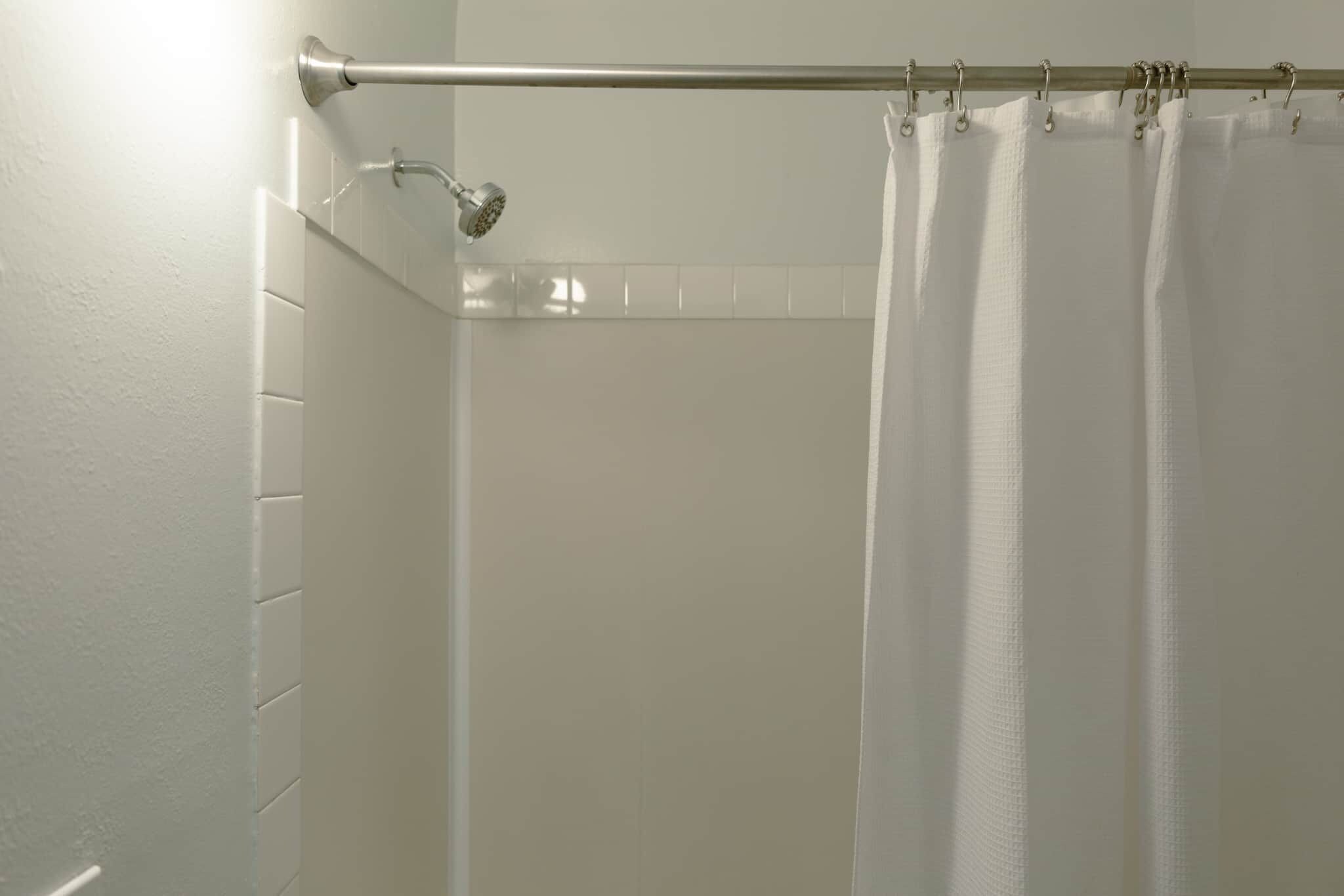 Un espace douche équipé d’une tringle à rideau en métal, d’un pommeau de douche et d’un rideau de douche blanc.