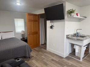 A hotel room with a bed, a TV mounted on the wall, a small sink, and a door leading to another room.
