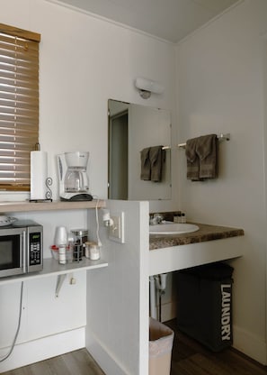 Una kitchenette compacta con microondas, cafetera y recipientes de almacenamiento.
