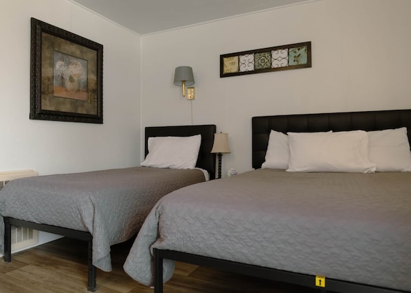 Quarto de hotel com duas camas, um quadro, uma luminária na parede e um azulejo decorativo.