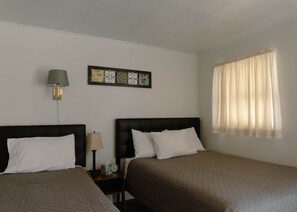 Una habitación de hotel con dos camas, una mesita de noche con lámpara, un reloj y una ventana con cortinas.