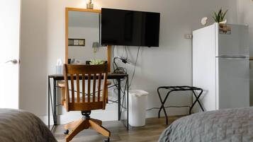 Habitación compacta con una silla de madera, un escritorio, un televisor montado en la pared, una mesita pequeña y un refrigerador.