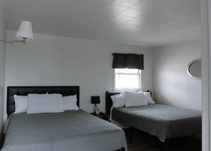 Une chambre avec deux lits, une fenêtre avec un rideau, un miroir rond et une lampe fixée au mur.
