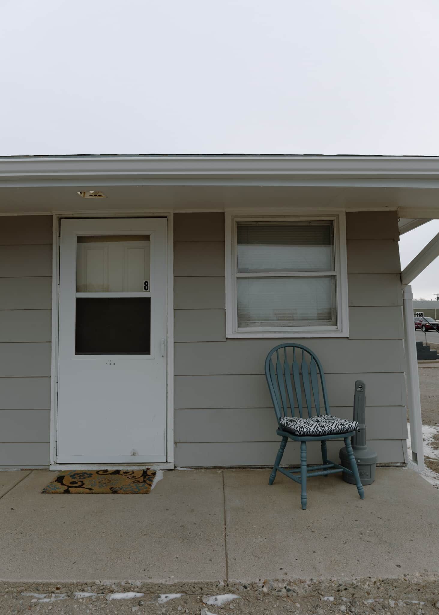 A house with a white door, a window, and a blue chair outside.