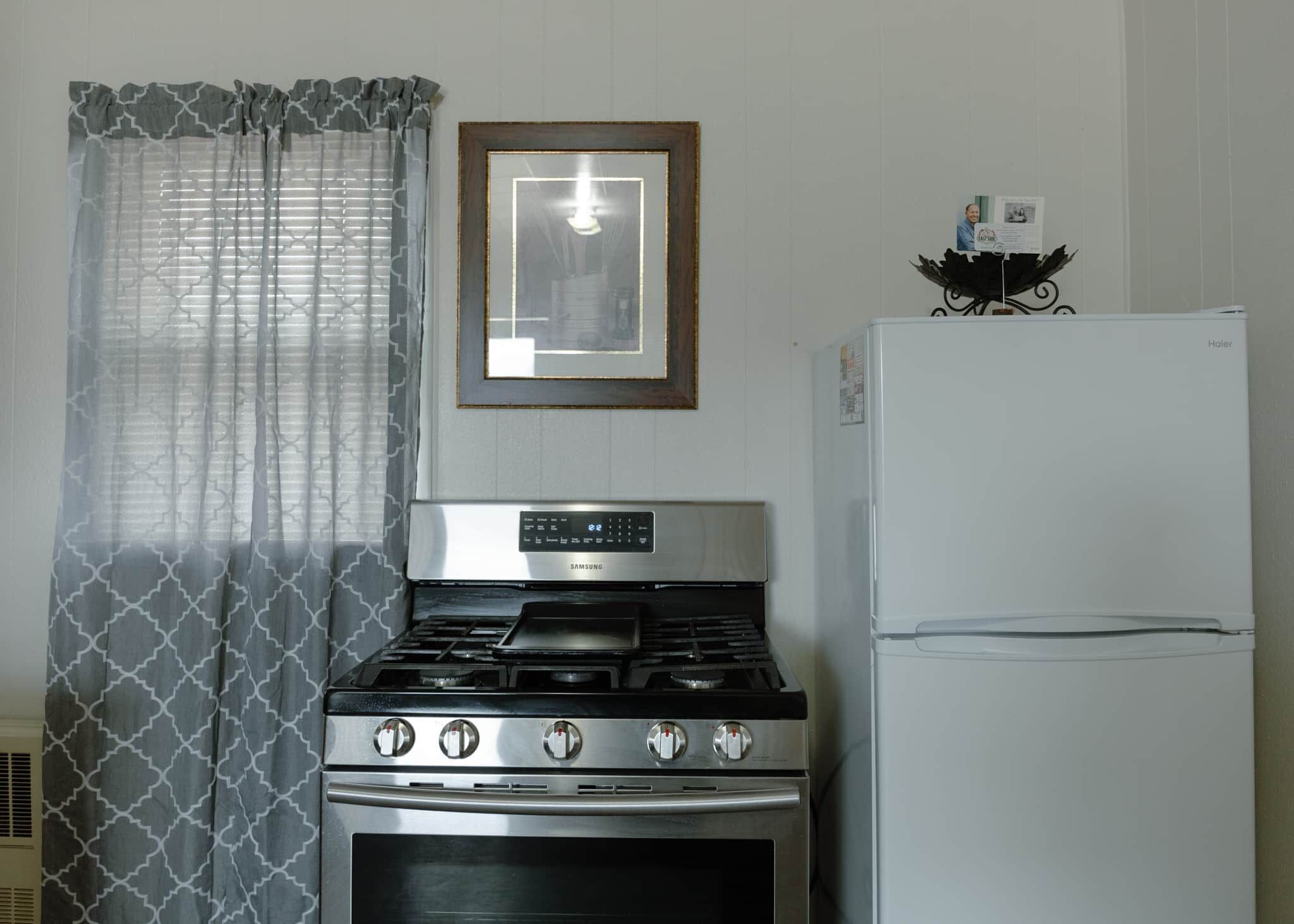 Una cocina con estufa a gas Samsung, un refrigerador blanco y cortinas estampadas.