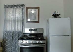 A kitchen with a Samsung gas stove, a white refrigerator, and patterned curtains.