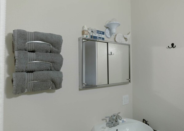A bathroom with a towel rack holding four towels, a mirror cabinet with a sign above it, and a sink with a faucet.
