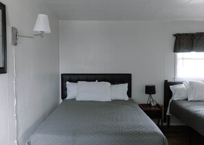 A single bed with a headboard, a bedside table with a lamp, and a window with curtains.