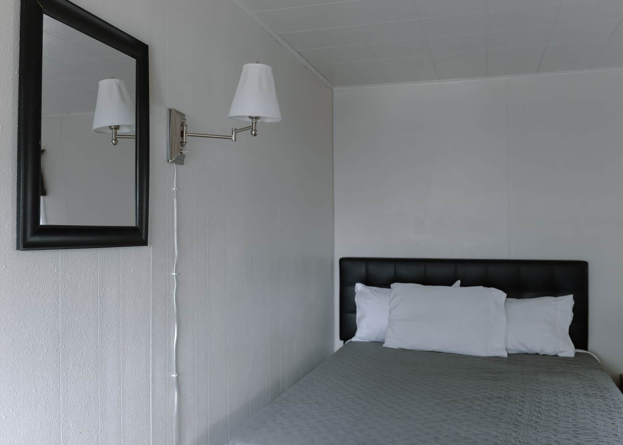Una habitación de hotel con una cama, una lámpara de pared y un espejo.