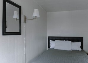 A hotel room with a bed, a wall-mounted light fixture, and a mirror.