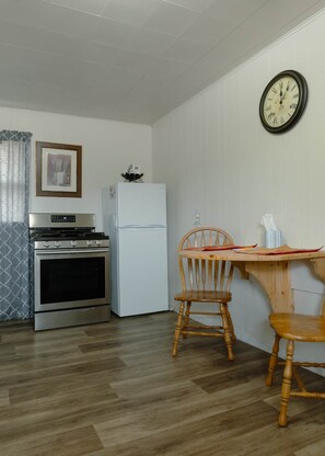 A compact kitchen with a stove, oven, refrigerator, and a wooden dining table with two chairs.
