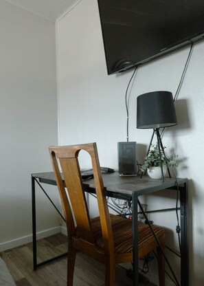 A room with a desk, a chair, a television mounted on the wall, and a lamp.