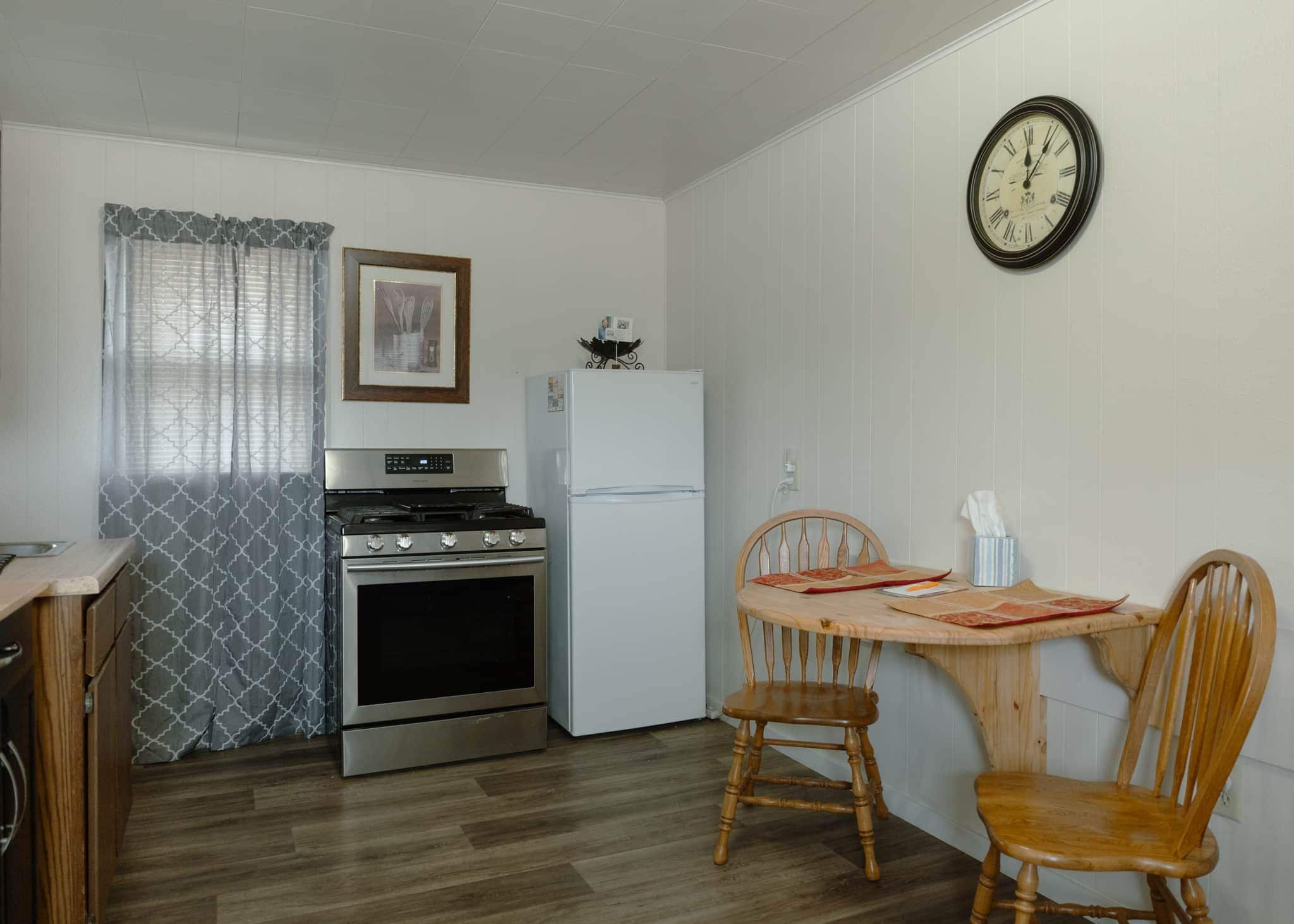 A compact kitchen with a stove, oven, refrigerator, and a dining table with chairs.