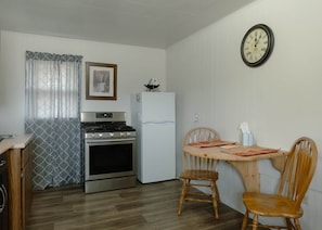 A compact kitchen with a stove, oven, refrigerator, and a dining table with chairs.