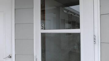 Een witte deur met het cijfer '5', een raam met hor en een witte buitenmuur.