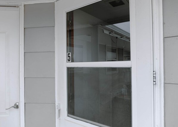 A white door with a number '5' on it, a window with a screen, and a white exterior wall.