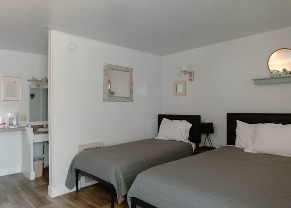 A bedroom with two beds, a bedside table, a mirror, and a small desk with a chair.