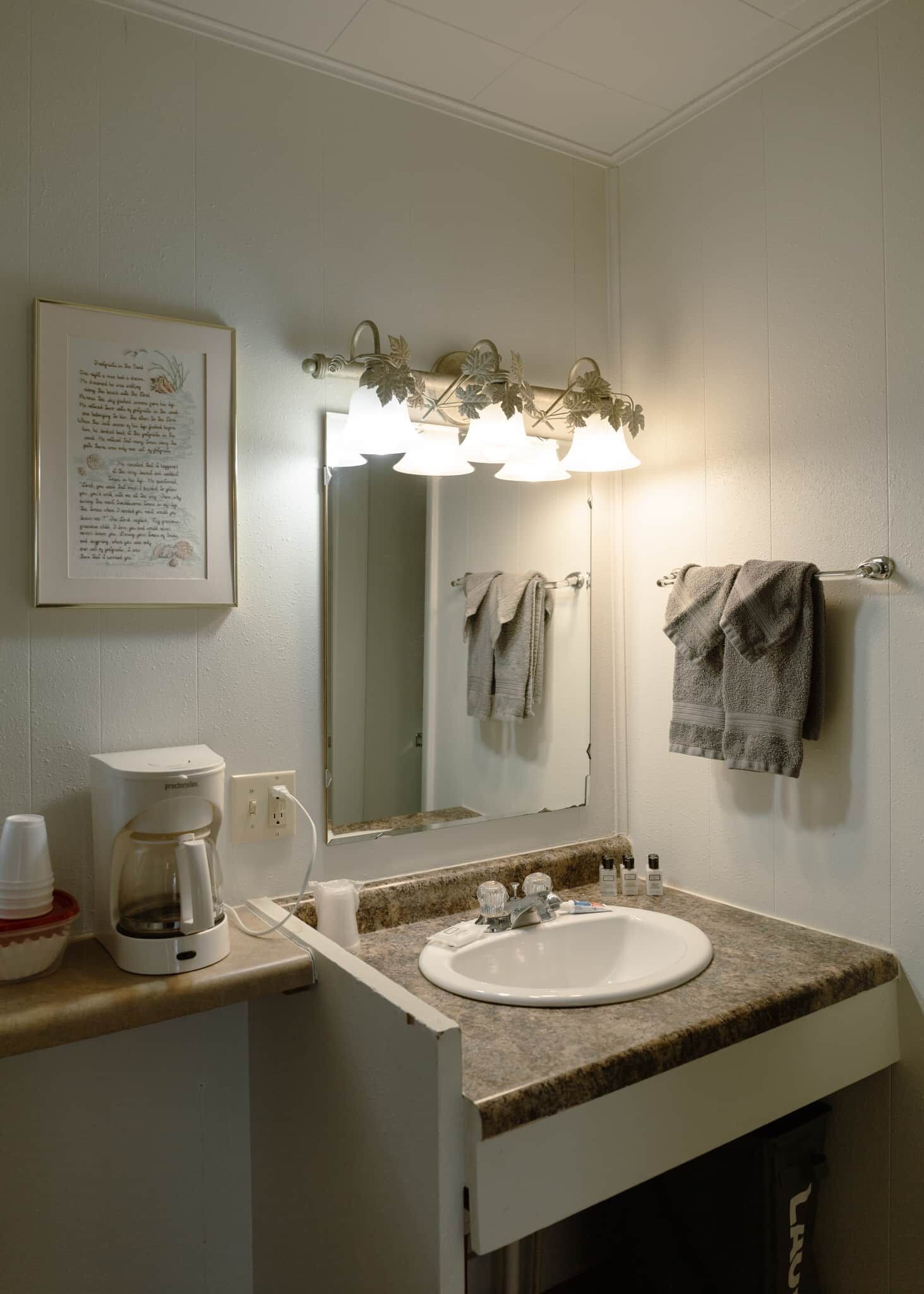 Une salle de bain avec un lavabo blanc, une machine à café, un miroir et un porte-serviettes.