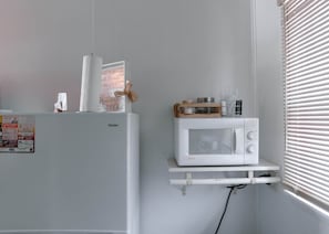 Cozinha com geladeira branca, micro-ondas em uma prateleira e janela com persianas.