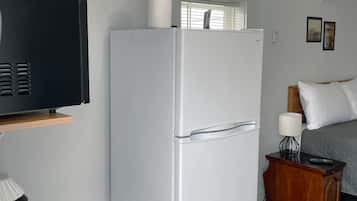 A compact kitchenette with a white refrigerator, a coffee maker, and a wooden shelf.