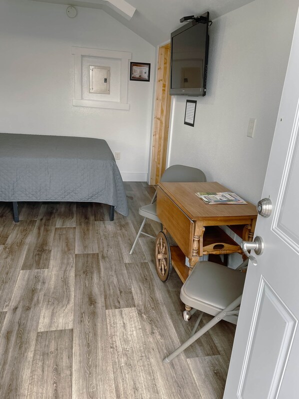 A bedroom with a bed, a desk with a chair, a television, and a door.