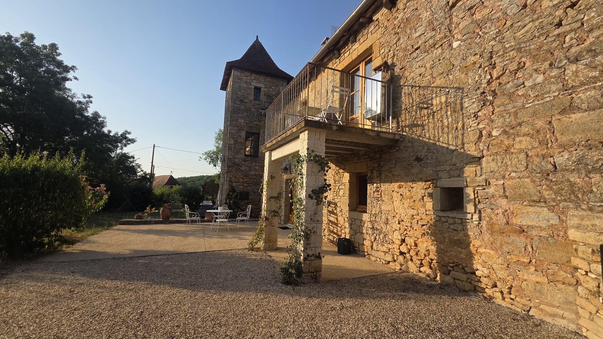 A stone building with a balcony, gravel ground, and a tower in the background.