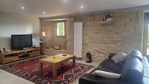 A living room with a stone wall, a television, a wooden coffee table, a sofa, and a patterned rug. - Vacation rental in the Périgord Noir region between Périgueux and Sarlat, featuring a heated Nordic bath, (Granges-d'Ans)