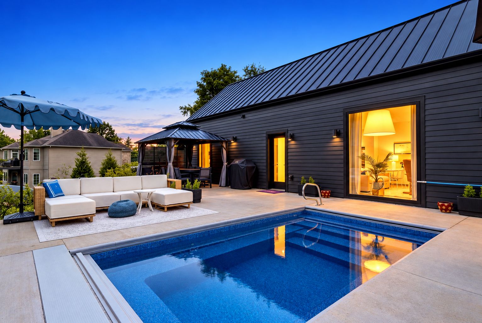 A modern outdoor pool area with a built-in hot tub, a covered seating area, and a well-lit entrance.