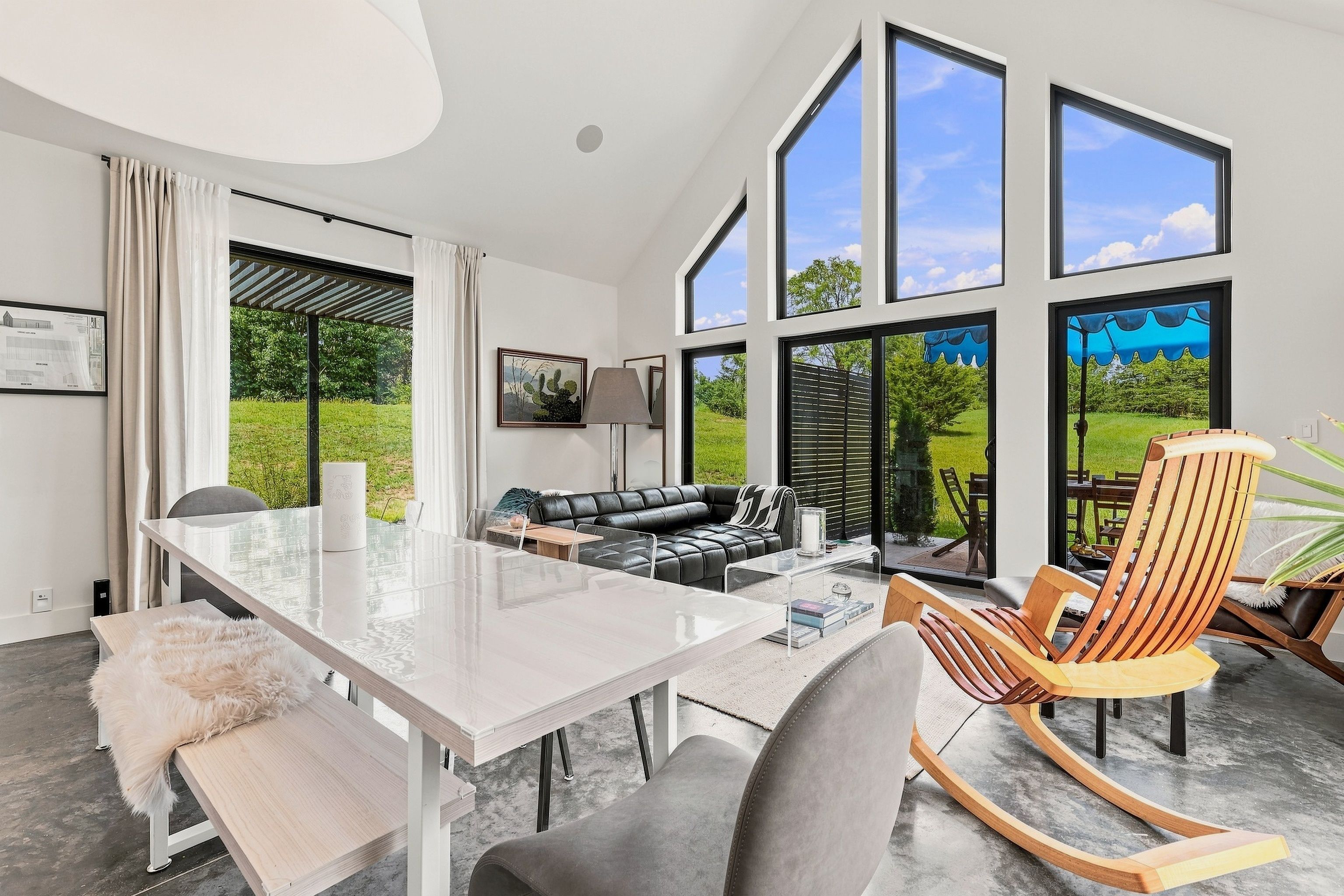 A modern living room with a glass dining table, leather sofa, and a wooden rocking chair.