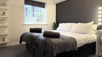 Une chambre moderne avec un lit, des tables de chevet, une fenêtre avec des stores et une vue sur les bâtiments environnants.