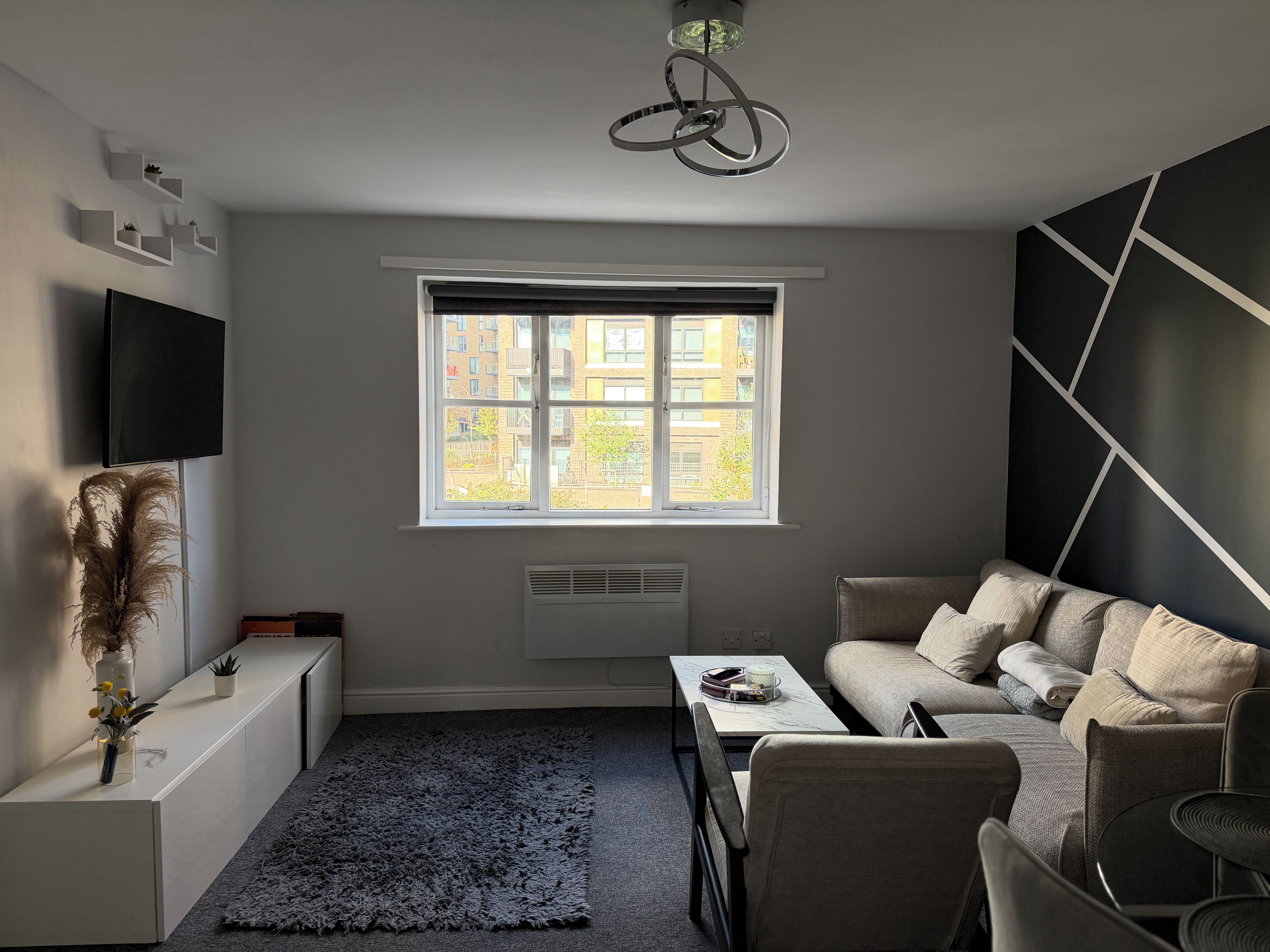 Un salon moderne avec un canapé, une table basse, un téléviseur et une fenêtre donnant sur des immeubles.