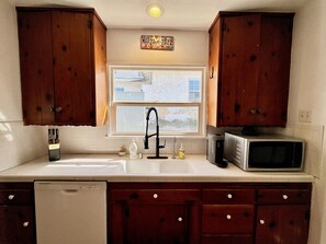 A kitchen with wooden cabinets, a stainless steel sink, a microwave, and a window above the sink. - Ocean View 3-brm House w/ Sauna, Fireplace & EV Charging (Hermosa Beach)