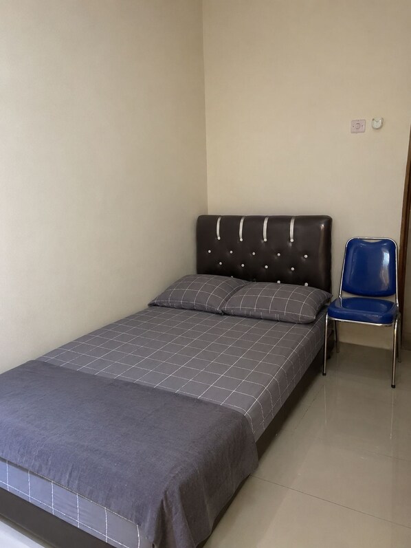 A single bed with a grey bedspread and two pillows, a blue chair, and a plain wall with a light switch. - Hotel O Pollux Mall Cikarang (Cikarang)