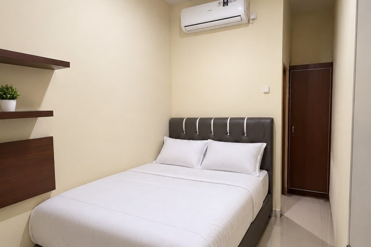 A hotel room with a bed, an air conditioning unit, a door, and a small plant on a shelf.