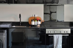 A modern kitchen with a black countertop, stainless steel appliances, and a wooden cutting board. - Trendy Studio Apartment at The Tokyo in Central Cape Town City (Cape Town)